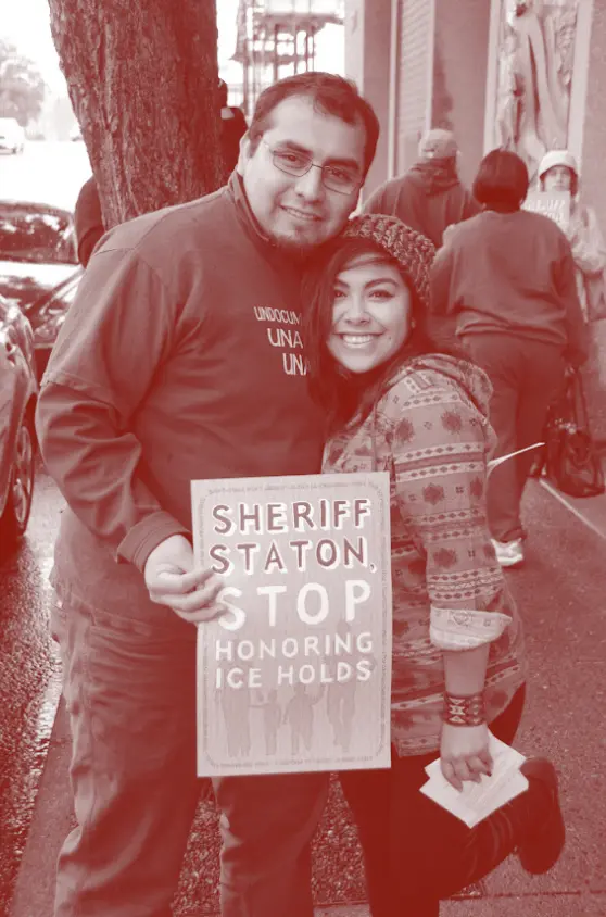 A man and woman holding a sign at a rally for immigrant rights.